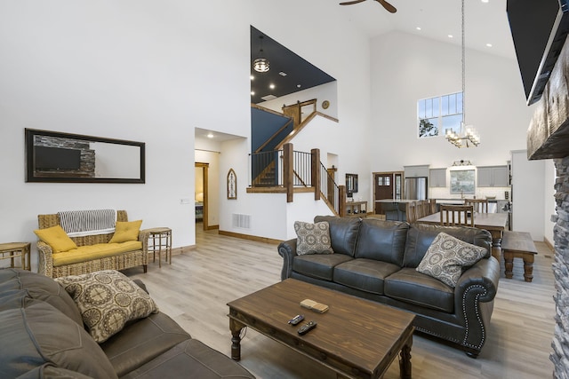 living room featuring ceiling fan with notable chandelier, visible vents, baseboards, stairway, and light wood-type flooring