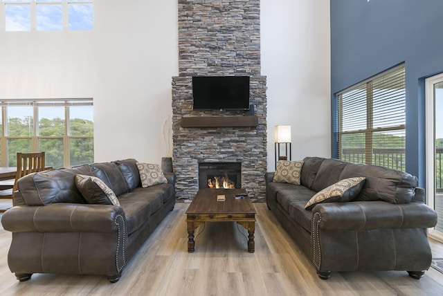 living room with a towering ceiling, light wood-style floors, a fireplace, and a healthy amount of sunlight