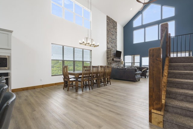 dining area featuring a chandelier, a towering ceiling, baseboards, stairs, and light wood-type flooring