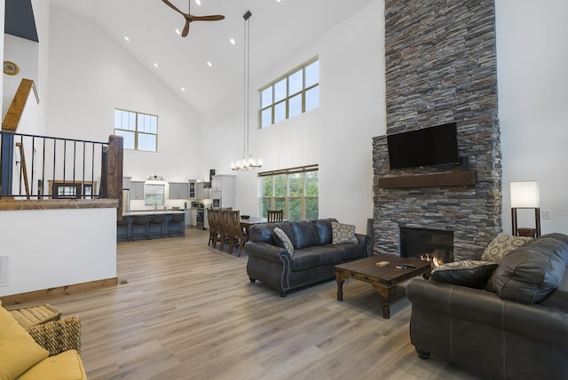 living room featuring light wood-style floors, a fireplace, visible vents, and ceiling fan with notable chandelier