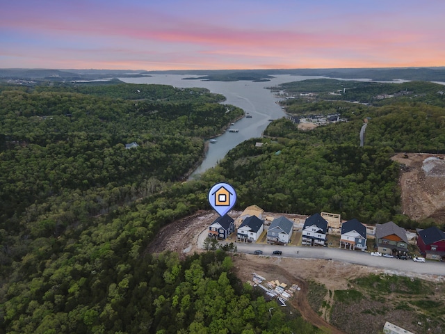 aerial view at dusk featuring a water view and a wooded view