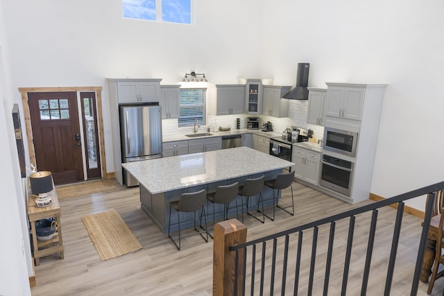 kitchen with a breakfast bar, a sink, appliances with stainless steel finishes, a center island, and wall chimney exhaust hood