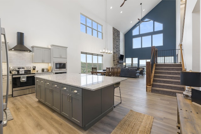 kitchen featuring stainless steel appliances, light wood-style flooring, gray cabinetry, plenty of natural light, and wall chimney exhaust hood