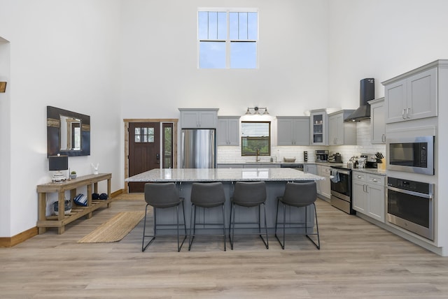 kitchen with appliances with stainless steel finishes, a kitchen island, wall chimney range hood, and gray cabinetry