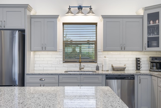 kitchen with appliances with stainless steel finishes, gray cabinets, a sink, and decorative backsplash