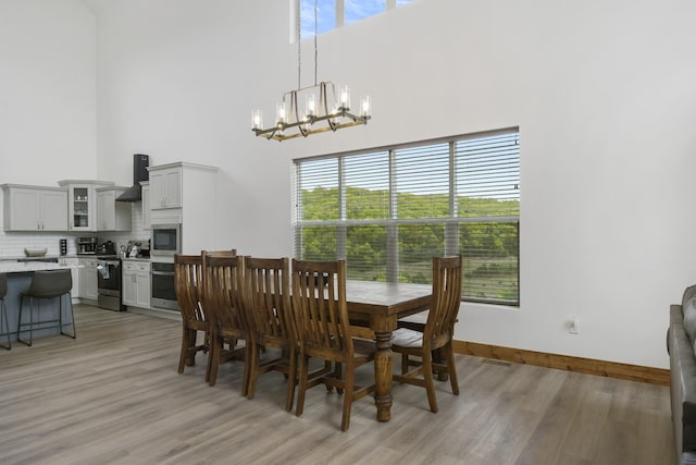 dining room with a chandelier, light wood-type flooring, a towering ceiling, and baseboards