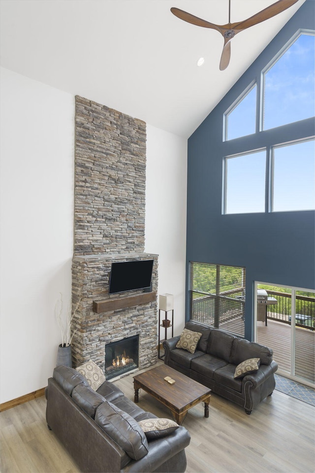 living room featuring baseboards, a ceiling fan, wood finished floors, a stone fireplace, and high vaulted ceiling