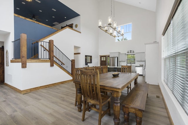 dining area featuring ceiling fan with notable chandelier, wood finished floors, visible vents, baseboards, and stairs