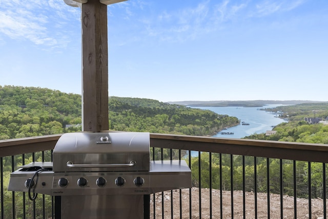 deck featuring a wooded view, a water view, and a grill