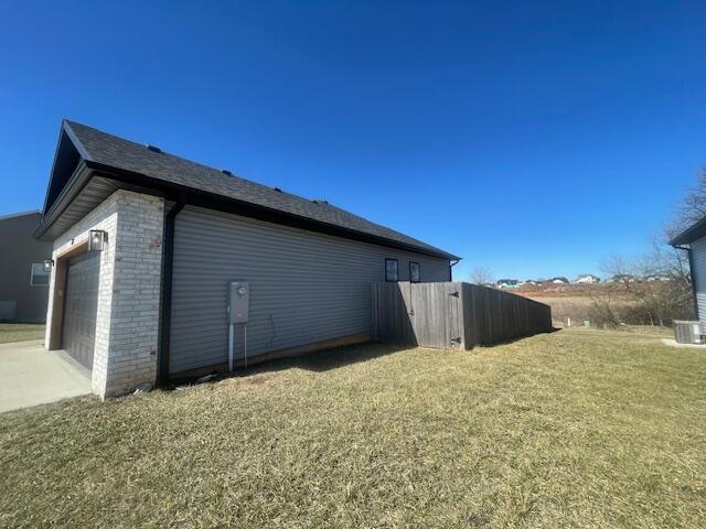 view of side of home featuring an attached garage, brick siding, a lawn, and central AC unit