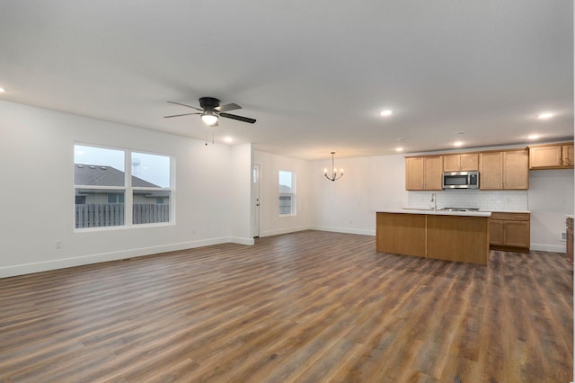 kitchen featuring ceiling fan with notable chandelier, dark wood-style flooring, open floor plan, backsplash, and stainless steel microwave