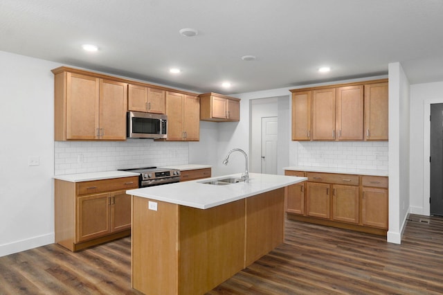 kitchen with dark wood-style flooring, a sink, light countertops, appliances with stainless steel finishes, and an island with sink