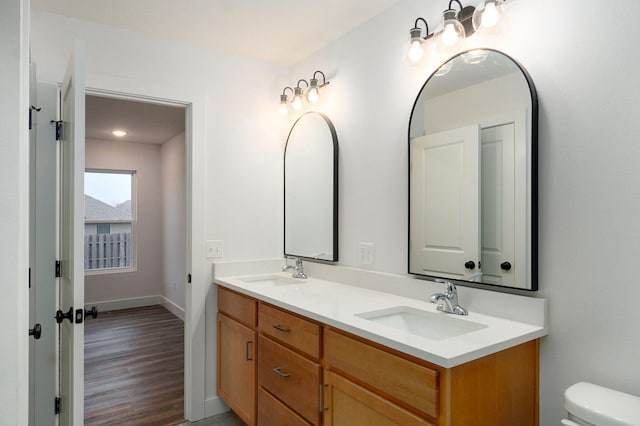 bathroom with double vanity, wood finished floors, a sink, and toilet