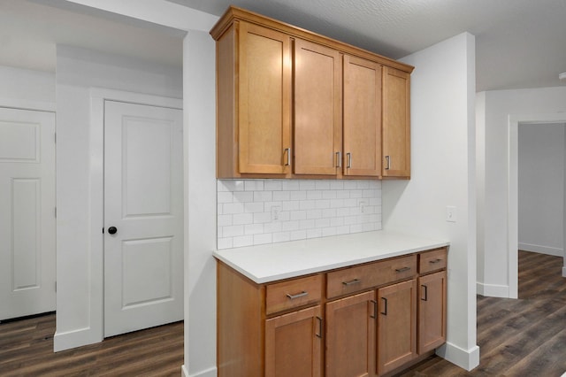 kitchen featuring dark wood-style flooring, brown cabinets, light countertops, decorative backsplash, and baseboards