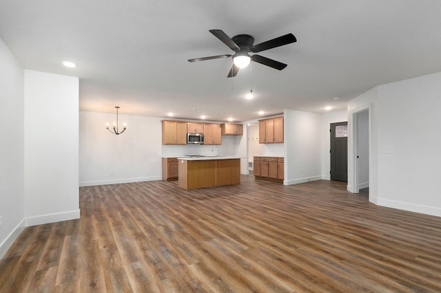 kitchen with a center island with sink, stainless steel microwave, open floor plan, dark wood-style flooring, and backsplash