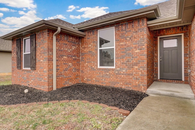 doorway to property featuring roof with shingles and brick siding