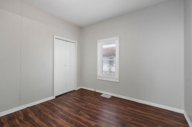 unfurnished bedroom with dark wood-type flooring, a closet, visible vents, and baseboards