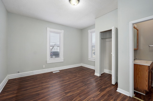 unfurnished bedroom featuring dark wood-style flooring, a closet, visible vents, a sink, and baseboards