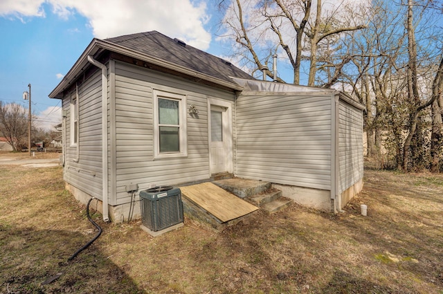 back of house with a shingled roof, a lawn, and cooling unit