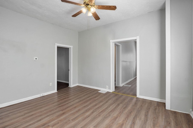 empty room with ceiling fan, a textured ceiling, baseboards, and wood finished floors