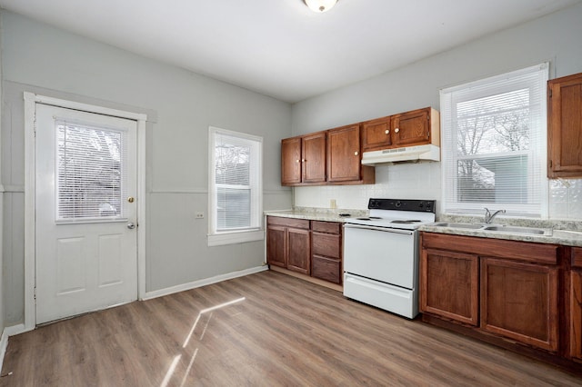 kitchen with white electric stove, light wood-style floors, brown cabinetry, a sink, and under cabinet range hood