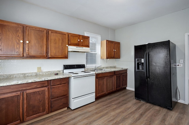 kitchen with under cabinet range hood, wood finished floors, a sink, electric stove, and black fridge