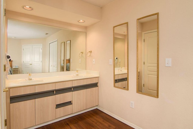 full bath with double vanity, wood finished floors, a sink, and baseboards