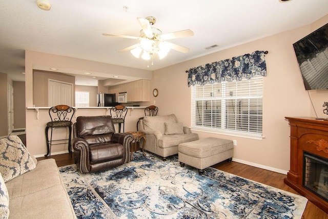 living area featuring a fireplace, wood finished floors, a ceiling fan, visible vents, and baseboards
