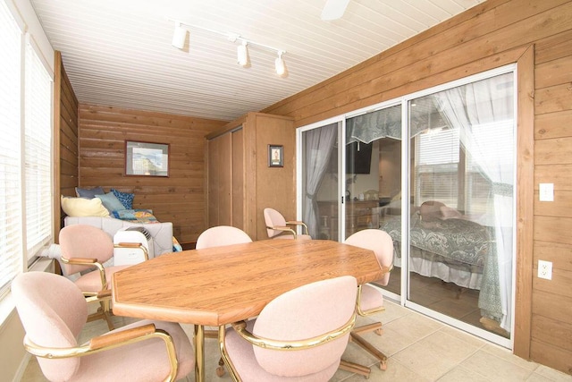 dining space featuring rail lighting, wooden walls, and light tile patterned floors