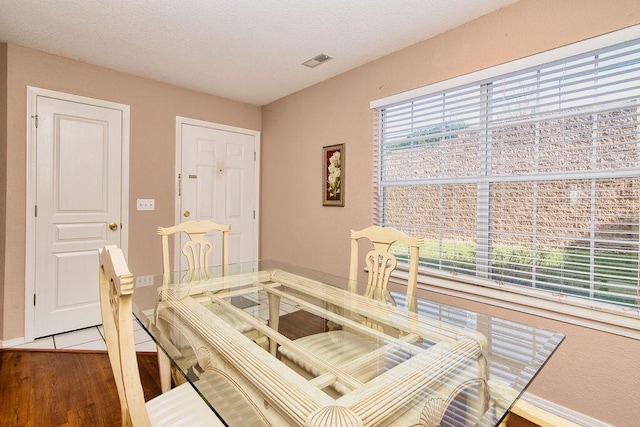 dining space featuring a textured ceiling, wood finished floors, visible vents, and baseboards