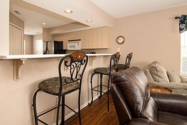 kitchen featuring white microwave, open floor plan, a kitchen breakfast bar, dark wood-style flooring, and freestanding refrigerator