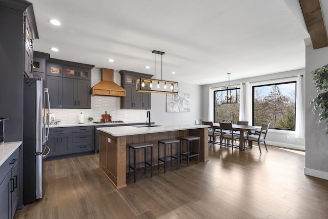 kitchen featuring dark wood finished floors, decorative backsplash, custom range hood, freestanding refrigerator, and a sink