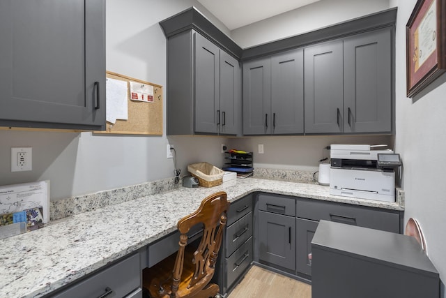 kitchen featuring built in desk, gray cabinets, light wood-style flooring, and light stone countertops