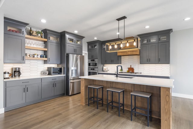 kitchen with light wood finished floors, stainless steel appliances, light countertops, a kitchen bar, and a sink