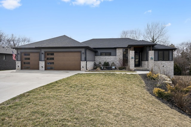 prairie-style house with a garage, a shingled roof, concrete driveway, stone siding, and a front yard