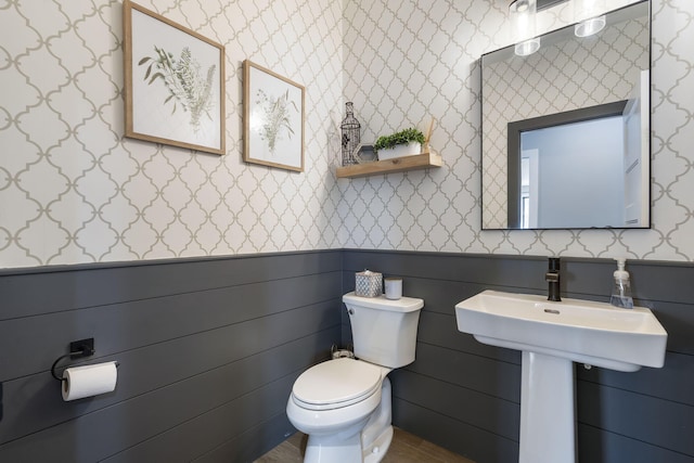 bathroom with toilet, wallpapered walls, and wainscoting