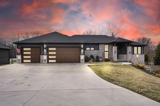 prairie-style home featuring concrete driveway, stone siding, roof with shingles, an attached garage, and a front lawn