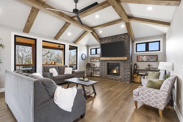 living area featuring lofted ceiling with beams, recessed lighting, a fireplace, wood finished floors, and baseboards