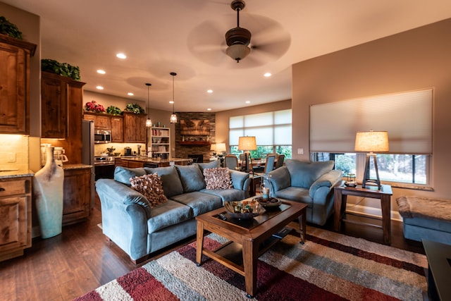 living room with dark wood-style floors, ceiling fan, a stone fireplace, and recessed lighting