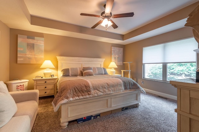 carpeted bedroom with a tray ceiling, a ceiling fan, and baseboards