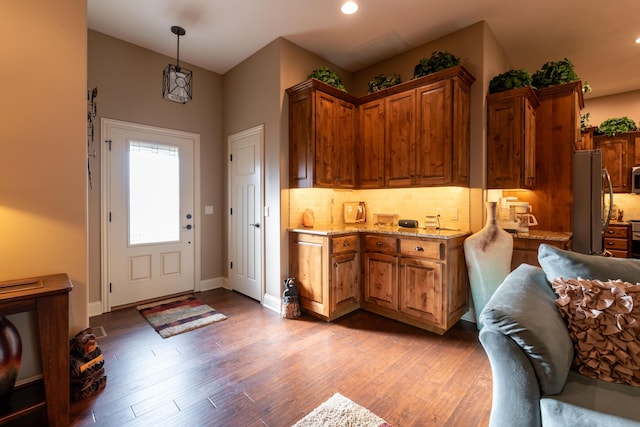 kitchen featuring baseboards, light wood-style floors, appliances with stainless steel finishes, backsplash, and brown cabinets