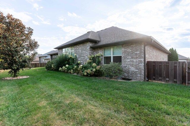 view of home's exterior featuring a yard, brick siding, fence, and roof with shingles