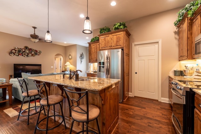 kitchen with arched walkways, brown cabinets, dark wood finished floors, appliances with stainless steel finishes, and a sink