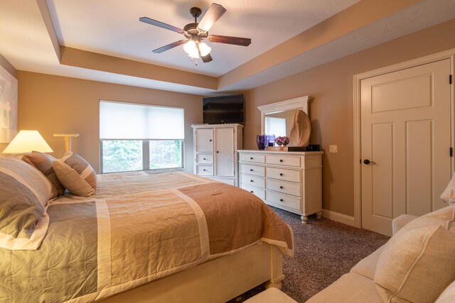 bedroom with carpet, a raised ceiling, ceiling fan, and baseboards