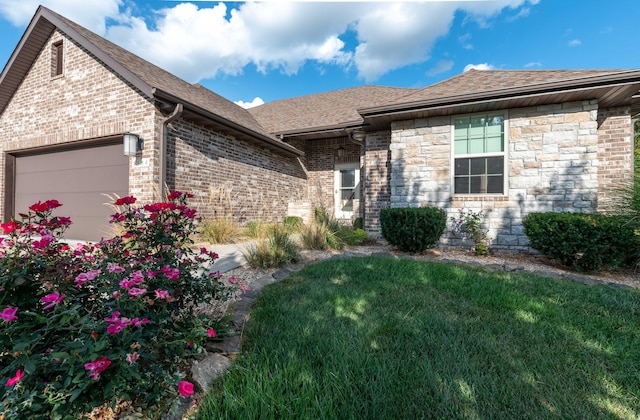 view of front of house featuring stone siding, roof with shingles, an attached garage, a front yard, and brick siding