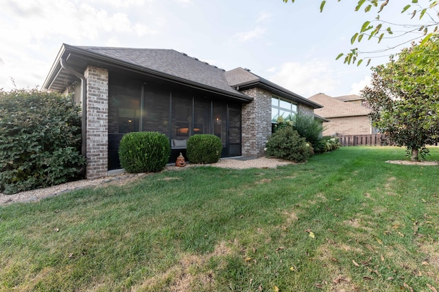 rear view of house featuring brick siding, a lawn, and fence