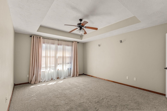 empty room featuring a raised ceiling, a textured ceiling, and baseboards