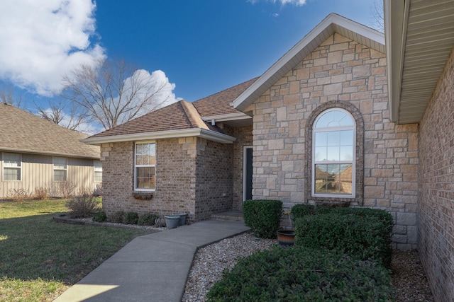 view of exterior entry with roof with shingles, a lawn, and brick siding