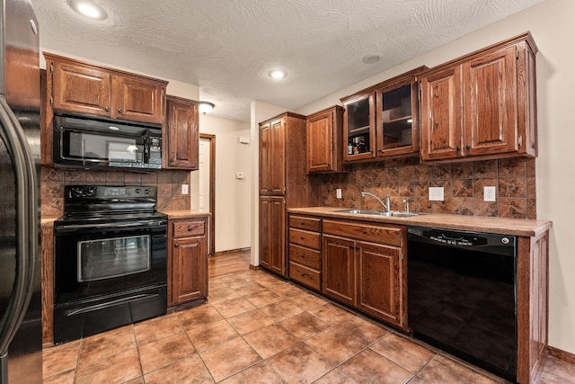 kitchen featuring decorative backsplash, glass insert cabinets, light countertops, black appliances, and a sink