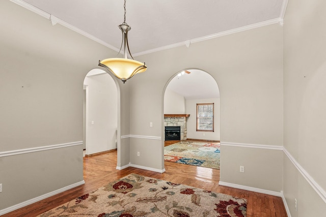 unfurnished dining area with baseboards, arched walkways, wood finished floors, and a stone fireplace